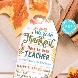May include: A printable Thanksgiving teacher appreciation gift tag with a white woodgrain background. The tag features a fall-themed design with leaves, pumpkins, and the text "Mr. Smith We're so Thankful You're our TEACHER You bring out the best in us! HAPPY THANKSGIVING! FROM THE 4TH GRADE CLASS".