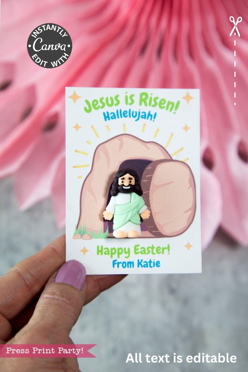 Pode incluir: Um cart&atilde;o branco com uma ilustra&ccedil;&atilde;o de desenho animado de Jesus saindo de um t&uacute;mulo, com o texto "Jesus ressuscitou! Aleluia!" e "Feliz P&aacute;scoa!" em verde e azul. O cart&atilde;o &eacute; segurado em uma m&atilde;o.