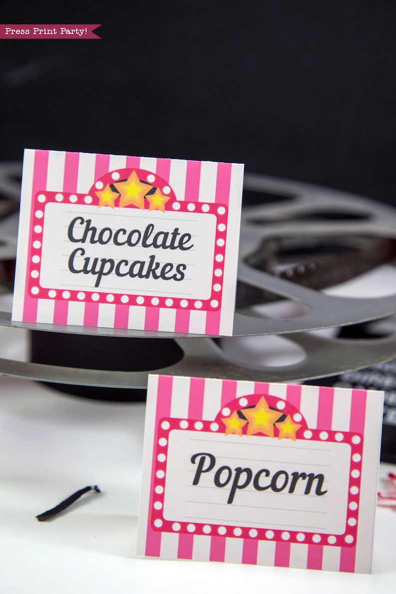 May include: Two pink and white striped signs with a marquee design and gold stars. The top sign says "Chocolate Cupcakes" and the bottom sign says "Popcorn".