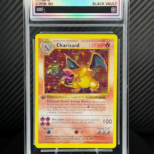 Puede incluir: Una carta Pokémon Charizard de 1999 PKMN TCG, 1ª edición Holo, calificada como MINT. Presenta una ilustración de Charizard amarillo y naranja con texto que describe sus habilidades.