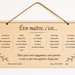 May include: A rectangular wooden sign with a rope hanger. The sign features French text in black, including phrases like "&Ecirc;tre ma&icirc;tre, c'est..." and "Merci pour votre engagement." Decorative floral elements are in the corners.
