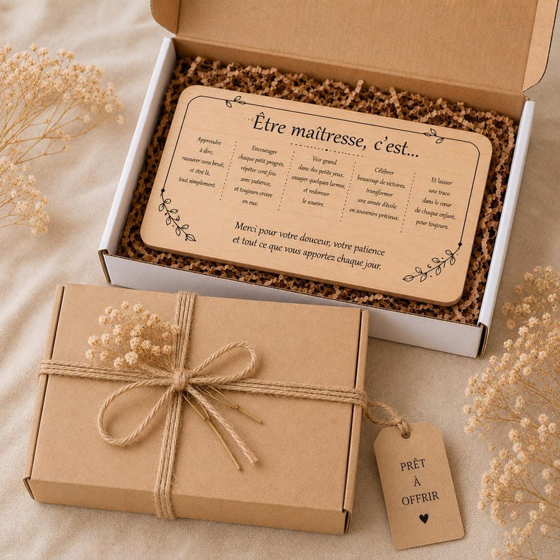 May include: A gift set featuring a wooden plaque with French text, presented in a cardboard box. The plaque reads "&Ecirc;tre ma&icirc;tresse, c'est..." and is decorated with floral accents. The box is tied with twine and a small tag.