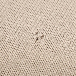 Pode incluir: Uma vista aproximada de um tecido de malha bege claro com um padr&atilde;o de ponto jersey consistente. Um pequeno pux&atilde;o ou fio solto &eacute; vis&iacute;vel perto do centro da imagem, interrompendo a textura uniforme do material tecido em malha.