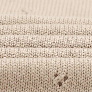Pode incluir: Uma vista aproximada de um tecido de malha bege claro com uma textura canelada consistente, apresentando colunas verticais de pontos entrela&ccedil;ados. O material exibe uma cor uniforme e uma apar&ecirc;ncia tecida suave com pequenos espa&ccedil;os subtis.