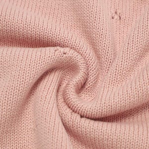 May include: A close-up view of a soft, light pink knitted fabric with a consistent stockinette stitch pattern. The material is gathered into a gentle swirl, highlighting the texture of the yarn loops and the uniform, matte finish of the textile.