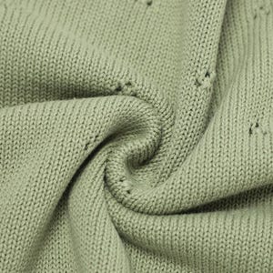 May include: A sage green knit fabric featuring a consistent stockinette stitch pattern with small, evenly spaced eyelet holes integrated into the weave. The material is folded into soft, deep pleats, highlighting the texture of the yarn.