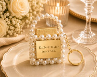 May include: A miniature handbag keychain crafted from white faux pearls with a gold-toned metal plate engraved with the text Emily & Taylor July 8, 2026. The accessory features a pearl-beaded handle and a gold metal ring attachment.