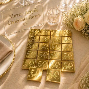 May include: Gold foil chocolate favors arranged on a table. Each chocolate square is embossed with the number "50" and the name "Leonardo" and the date "04.04.24". A clear acrylic sign reads "Mirror Acrylic Chocolate Favors".