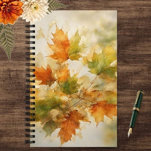 May include: A spiral-bound notebook featuring a watercolor-style illustration of autumn maple leaves in shades of orange, yellow, and green. The cover design displays a layered, textured appearance with visible leaf veins and soft color blending.