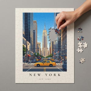 Può includere: Un puzzle a tema New York City, con l'Empire State Building e taxi gialli. Il puzzle è quasi completo, con una mano che aggiunge l'ultimo pezzo. Le parole "NEW YORK" sono stampate in basso.