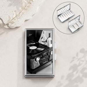 May include: A rectangular silver metal case featuring a black and white graphic of a vintage record player and bottles on the front. The case has a hinged lid and includes an internal compartment with dividers for organizing small items.