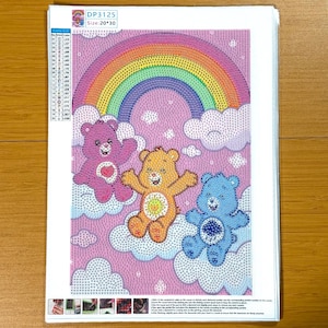 May include: A diamond painting kit featuring three colorful Care Bears floating on clouds under a rainbow. The image is 20 x 30 inches in size. The bears are pink, orange, and blue, each with a unique belly badge.