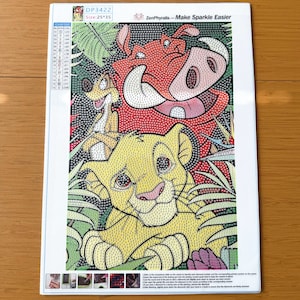 May include: A diamond painting kit featuring a printed canvas with a numbered grid design of a lion cub, a meerkat, and a warthog. The top includes the text ZenPhyralis - Make Sparkle Easier, a color list, and a size label of 25x35 inches.