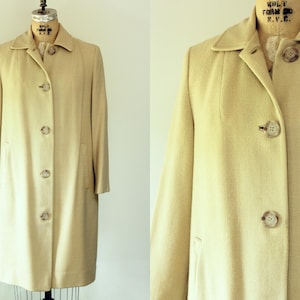 Puede incluir: Un abrigo beige vintage con un dise&ntilde;o cl&aacute;sico. El abrigo presenta un cuello, mangas largas y una botonadura frontal. Tiene un corte entallado y dos bolsillos delanteros. El abrigo se exhibe en un maniqu&iacute;.