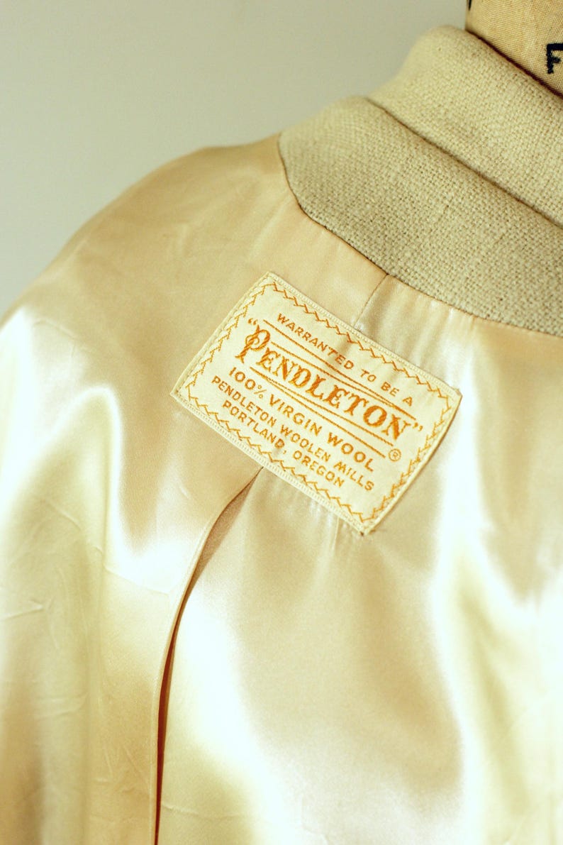 Puede incluir: Primer plano del forro de sat&eacute;n color crema de una chaqueta, con cuello beige. Una etiqueta rectangular dice "PENDLETON" y "100% Virgin Wool, Pendleton Woolen Mills, Portland, Oregon."