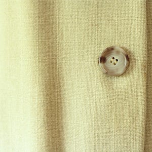Puede incluir: Primer plano de una tela beige claro con un bot&oacute;n redondo veteado. El bot&oacute;n tiene un dise&ntilde;o en espiral marr&oacute;n claro y crema y tres peque&ntilde;os agujeros. La tela tiene un aspecto texturizado.