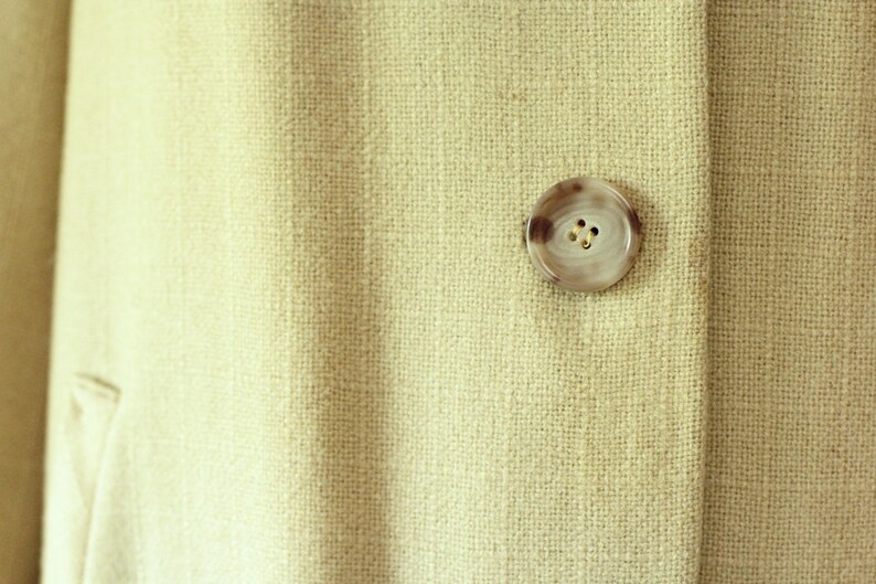 Puede incluir: Primer plano de una tela beige claro con un bot&oacute;n redondo veteado. El bot&oacute;n tiene un dise&ntilde;o en espiral marr&oacute;n claro y crema y tres peque&ntilde;os agujeros. La tela tiene un aspecto texturizado.
