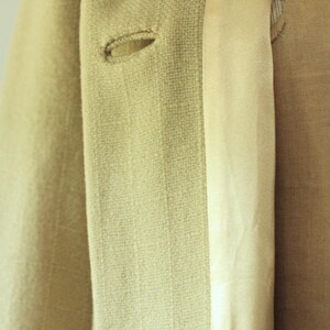 Puede incluir: Primer plano de una blazer beige claro con dos ojales visibles. La blazer tiene una tela texturizada y un forro satinado. La imagen destaca los detalles de la confecci&oacute;n.