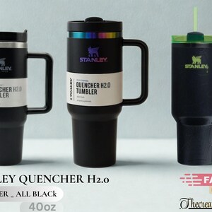 May include: Three black Stanley Quencher H2.0 tumblers with handles and straws. The two left tumblers feature white product labels reading Quencher H2.0 Tumbler. The center tumbler has an iridescent rim, and the right tumbler has a green lid.