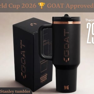 May include: A matte black insulated tumbler with a handle and a black lid, featuring the word GOAT in metallic copper lettering on the side. The tumbler is displayed next to its matching black box, which also features the GOAT logo in copper.