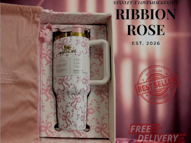 Puede incluir: Un vaso Stanley blanco con un patr&oacute;n de lazos rosas, un logotipo dorado y una tapa rosa claro. El vaso se presenta en una caja a juego con una bolsa de tela rosa. El texto en la caja dice Stanley x LoveShackFancy, Ribbon Rose, Est. 2026.