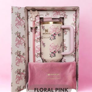 May include: A cream-colored Stanley tumbler with a pink floral and bow pattern, featuring a matching pink straw with a bow topper and a pink velvet pouch, all housed in a decorative box with the same floral print and the text FLORAL PINK.