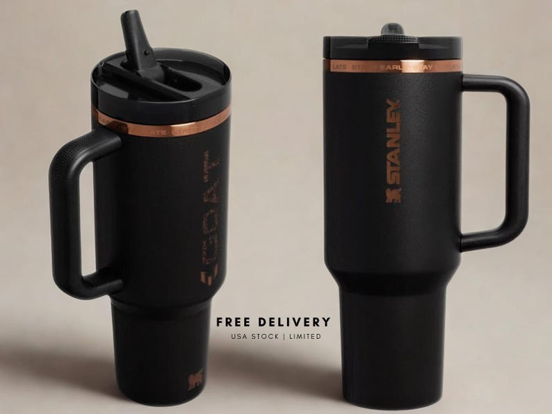 May include: Two matte black tumblers with handles and black lids. One tumbler features a straw and the text GOAT vertically, while the other displays the Stanley logo. Both have a copper-coloured band near the top rim and a tapered base design.