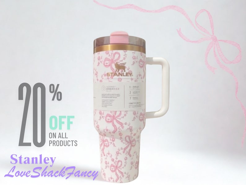 K&ouml;nnte beinhalten: Ein wei&szlig;er Stanley-Becher mit rosa Schleifen- und Blumenmuster, ausgestattet mit einem goldenen Rand, einem rosa Deckel und einem wei&szlig;en Henkel. Ein Produktetikett ist vorne angebracht. Der Text lautet 20% OFF ON ALL PRODUCTS und Stanley LoveShackFancy.