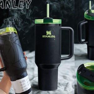May include: A black 40 oz insulated tumbler with a spiderweb pattern, a lime green lid, and a matching straw. The Stanley logo is printed in lime green on the front. The tumbler features a large side handle and a rotating lid mechanism.