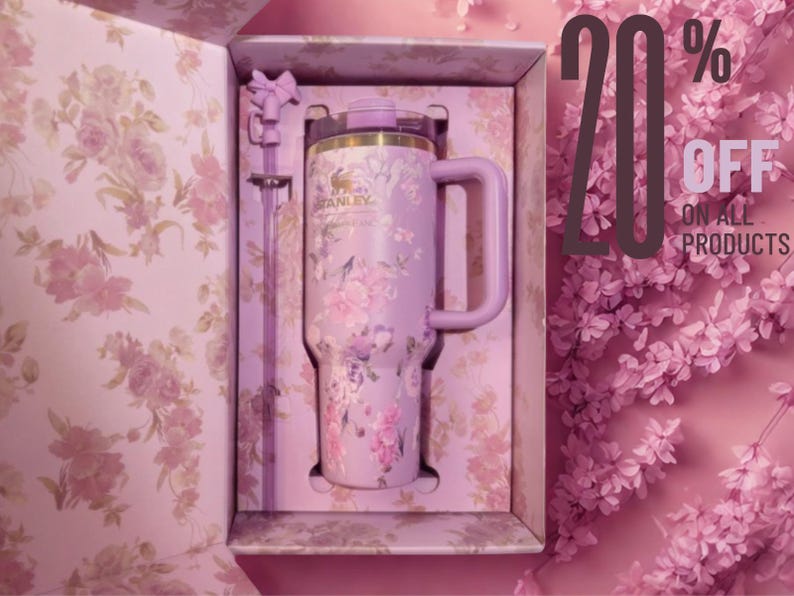 May include: A light purple Stanley tumbler with a floral pattern, a matching handle, and a straw, presented in a decorative box with a floral interior. The text 20% OFF ON ALL PRODUCTS is visible on the right side of the image.