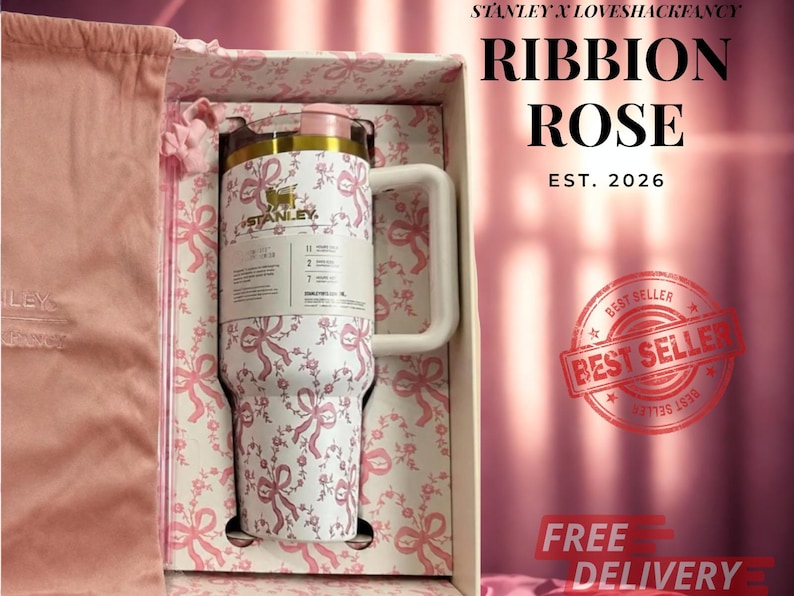 Puede incluir: Un vaso Stanley blanco con un patr&oacute;n de lazos y flores rosas, con un logotipo dorado, una tapa rosa claro y un asa color crema. El vaso se presenta en una caja a juego junto a una bolsa de tela rosa, con el texto que dice RIBBION ROSE.