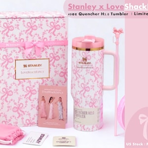 K&ouml;nnte beinhalten: Ein 1,18-Liter Stanley x LoveShackFancy Quencher H2.0 Becher mit einem rosa-wei&szlig;en Schleifenmuster, einem passenden rosa Strohhalm mit Schleifenaufsatz, einer Geschenkbox mit rosa Schleife, einem kleinen rosa Beutel und Infokarten mit Markentext.