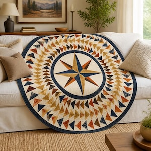 May include: A round quilt with a compass rose design, featuring a navy blue border and a cream-colored center. The compass rose is in shades of blue, orange, and brown. The quilt is covered in triangles in shades of brown, orange, and cream.