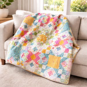 May include: A colorful patchwork quilt draped over a beige sofa. The quilt features a mix of floral and geometric patterns in shades of pink, yellow, blue, and green. The quilt is made of various fabric squares and shapes.