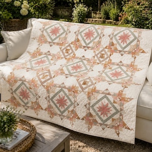 Peut inclure: Une couverture crème ornée d'un motif géométrique d'étoiles roses, pêche et vertes. La couverture est posée sur un canapé blanc à l'extérieur, mettant en valeur son design complexe. Les dimensions de la couverture ne sont pas visibles.