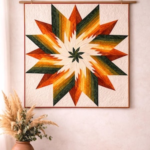 Puede incluir: Un edredón para colgar en la pared con un diseño de estrella. La estrella presenta un degradado de tonos naranja, amarillo y verde que irradian desde una estrella verde central. El edredón está enmarcado en un borde de madera y suspendido de una barra de madera.