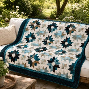 May include: A quilt featuring a repeating star pattern in shades of deep teal, light blue, and earthy brown against a cream background. The textile has a dark teal border and is draped over a white sofa, showcasing intricate stitching throughout.