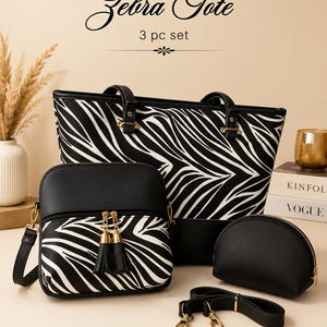 May include: A 3-piece bag set labelled Zebra Tote, featuring a large tote, a crossbody bag, and a small pouch. Each piece displays a black and white zebra stripe pattern with solid black accents, gold-tone hardware, and black tassel zipper pulls.