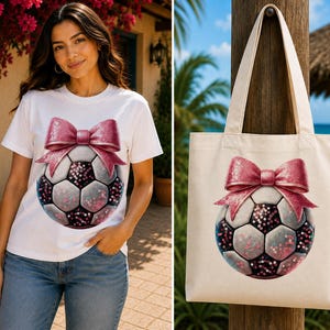 Puede incluir: Una camiseta blanca y una bolsa de tela a juego, ambas con un estampado gráfico de un balón de fútbol adornado con un gran lazo rosa brillante. El diseño del balón incorpora paneles oscuros y claros con lentejuelas rosas centelleantes.