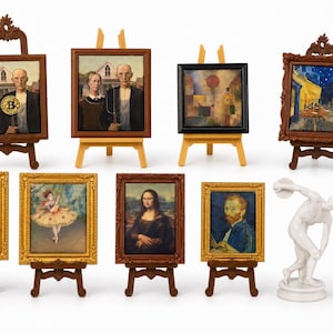 May include: A collection of eight miniature framed art prints displayed on small wooden easels, featuring famous paintings like American Gothic, the Mona Lisa, and Starry Night, alongside two small white statues of a discus thrower and a draped figure.