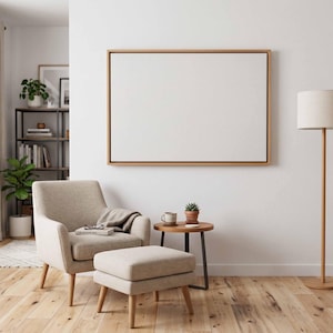 May include: A neutral-toned living room scene featuring a beige armchair, ottoman, and a small round side table. A large, blank canvas hangs on the wall above the chair. A floor lamp with a beige shade and a wooden base stands nearby.
