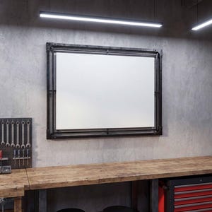 May include: A rectangular white board framed in black metal mounted on a concrete wall above a wooden workbench. The workspace includes a black pegboard with various hand tools, a metal shelving unit with storage bins, and a red metal tool chest.