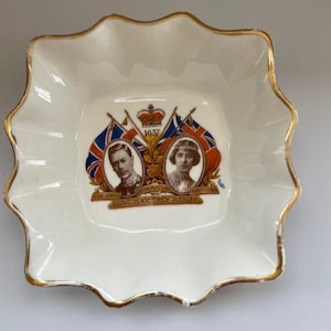May include: A white porcelain dish with a scalloped edge and gold trim. The centre features a 1937 coronation graphic with portraits of King George VI and Queen Elizabeth, flanked by Union Jack flags, a crown, and the text Long May They Reign.
