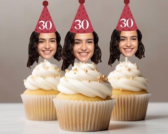 May include: Three cupcakes with white frosting and gold sprinkles. Each cupcake has a face on a stick wearing a red party hat with the number 30. The cupcakes are in white paper liners.