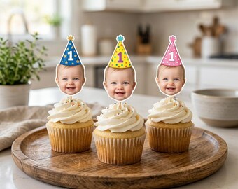 May include: Three cupcakes with white frosting and colorful sprinkles sit on a wooden tray. Each cupcake has a photo of a baby with a party hat that says "1". The hats are blue, yellow, and pink.