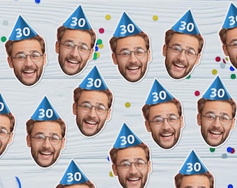 May include: A repeating pattern of smiling faces wearing blue party hats with the number 30. The faces are of a man with glasses and a beard. Colorful confetti is scattered around the faces on a light wood-grain background.