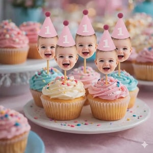 May include: Cupcakes with blue, pink, and white frosting, topped with sprinkles and baby face decorations wearing pink party hats with the number 1. Ideal for a first birthday, the cupcakes are arranged on a white plate.