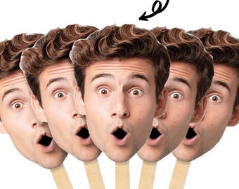 May include: Custom face masks featuring a surprised face, held by a wooden stick. The masks are printed with a man's face, with brown hair and wide eyes. The text "Custom Face Masks" is in blue, and the quantity options are listed below.