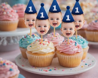 May include: Cupcakes with colorful frosting and sprinkles are arranged on a white plate. Each cupcake is topped with a smiling baby face wearing a blue party hat with the number 1. The background features more cupcakes.