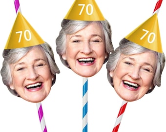 May include: Three party decorations featuring a smiling woman's face with a yellow party hat that has the number 70 on it. The faces are attached to colorful striped straws. The straws are pink and white, blue and white, and red and white.